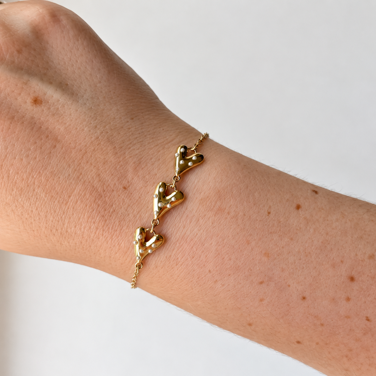 Armband met drie hartjes en witte details – goudkleurig gedragen aan de pols