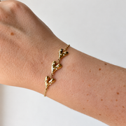 Armband met drie hartjes en witte details – goudkleurig gedragen aan de pols