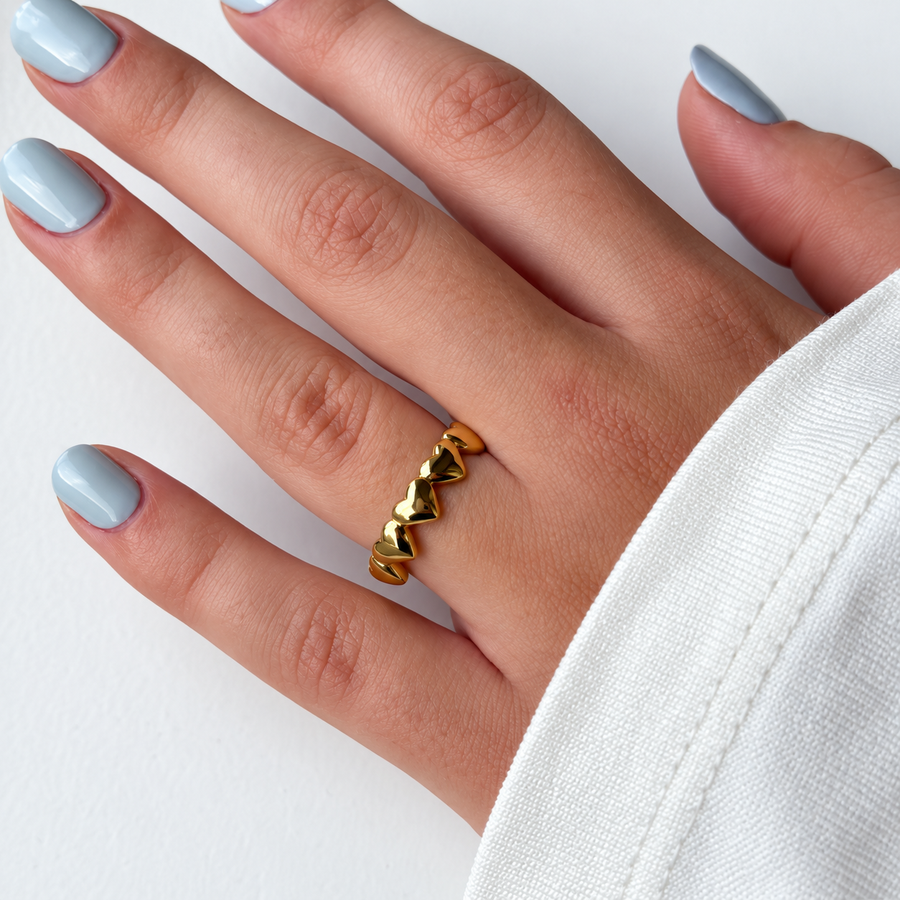Goudkleurige ring met rij hartjes gedragen aan de hand